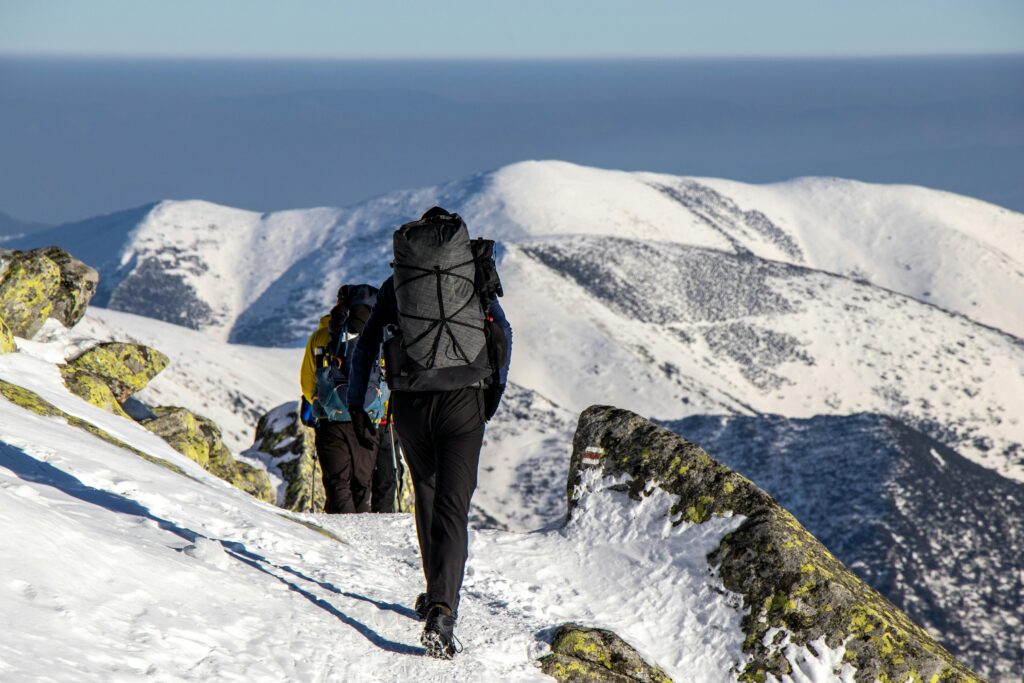 Hikers with backpacks trek through snow-covered mountains on a sunny winter day.